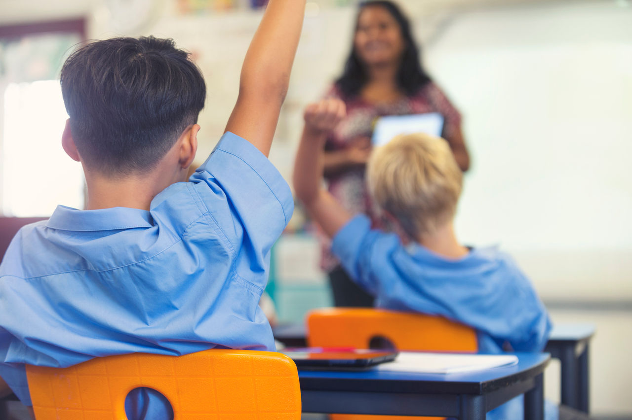 Aboriginal Elementary school  teacher giving a presentation to the class. The students have their hands raised to ask  questions in the classroom